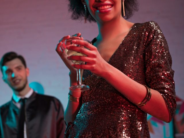 African american woman holding glass with cocktail by man at party